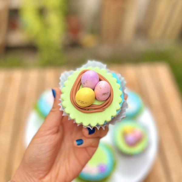 Encantadores cupcakes temáticos de Pascua decorados con conejitos, huevitos y zanahorias en fondant sobre un frosting celeste.