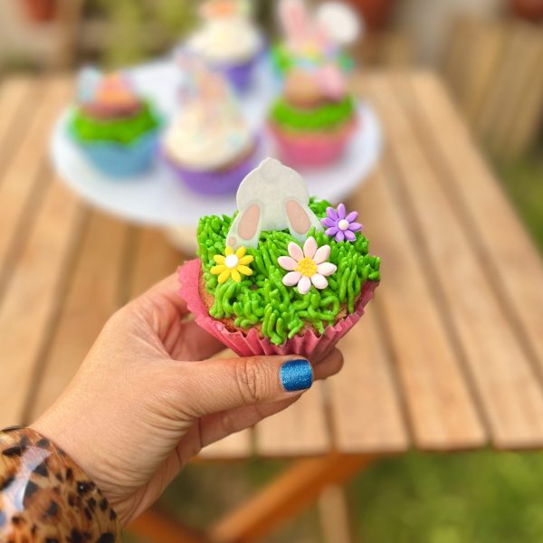Encantadores cupcakes temáticos de Pascua decorados con conejitos, huevitos y zanahorias en fondant sobre un frosting celeste.