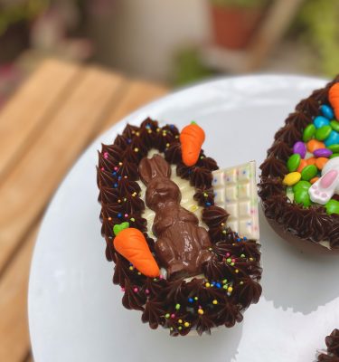 Irresistible huevo de Pascua con delicioso chocolate blanco mezclado con chispas de colores y encantadora decoración de zanahorias y conejitos de chocolate.