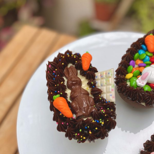 Irresistible huevo de Pascua con delicioso chocolate blanco mezclado con chispas de colores y encantadora decoración de zanahorias y conejitos de chocolate.