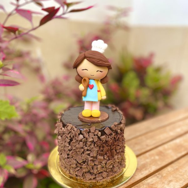 Encantadora mini torta de chocolate decorada con una figura de mamá cocinera y un topper dorado para celebrar el Día de la Madre.
