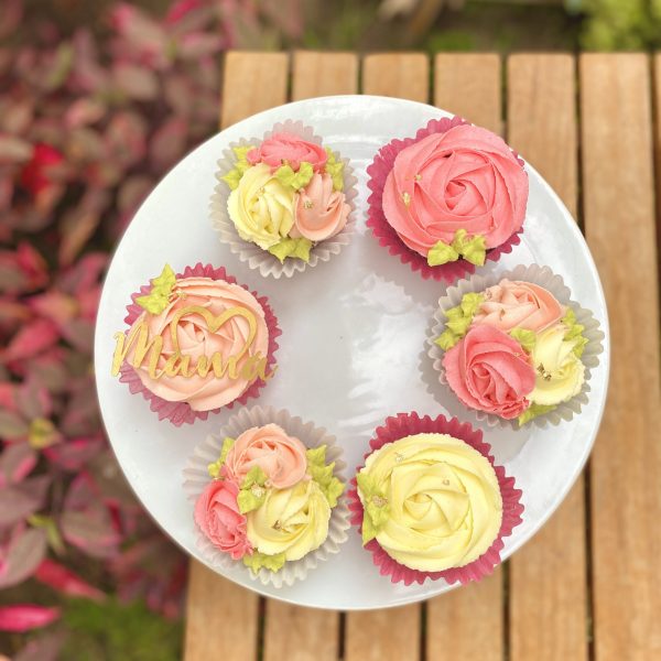 Seis cupcakes decorados con rosetones de buttercream y topper de Mamá con medio corazón.