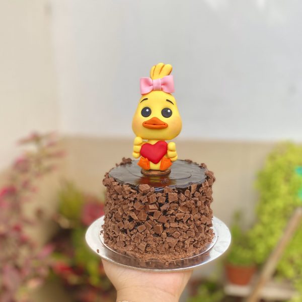 Encantadora mini torta de chocolate decorada con un adorable patito y un corazón dorado para celebrar el Día de la Madre.