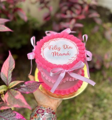 Mini Burncake Coquette decorada con buttercream y lazo coquette, con una oblea especial para el Día de la Madre, empaquetada en una caja blanca con ventana.
