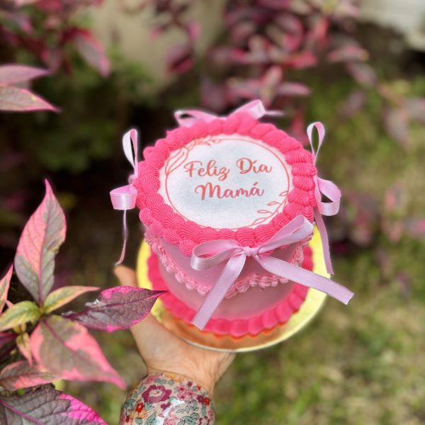 Mini Burncake Coquette decorada con buttercream y lazo coquette, con una oblea especial para el Día de la Madre, empaquetada en una caja blanca con ventana.
