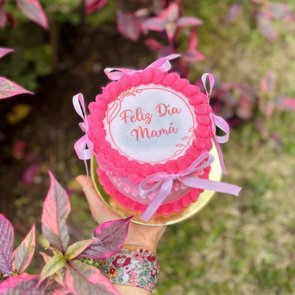 Mini Burncake Coquette decorada con buttercream y lazo coquette, con una oblea especial para el Día de la Madre, empaquetada en una caja blanca con ventana.