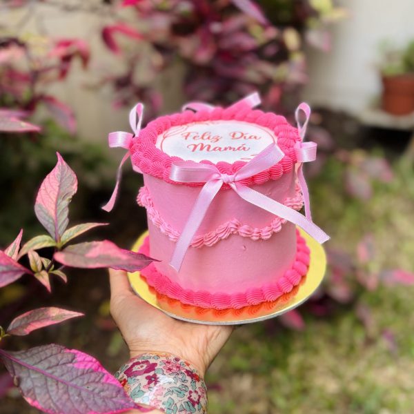 Mini Burncake Coquette decorada con buttercream y lazo coquette, con una oblea especial para el Día de la Madre, empaquetada en una caja blanca con ventana.