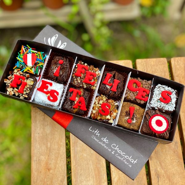 Doce brownies decorados con fondant y detalles de escarapela, presentados en una caja de diseño marrón vintage con lazo de tela.