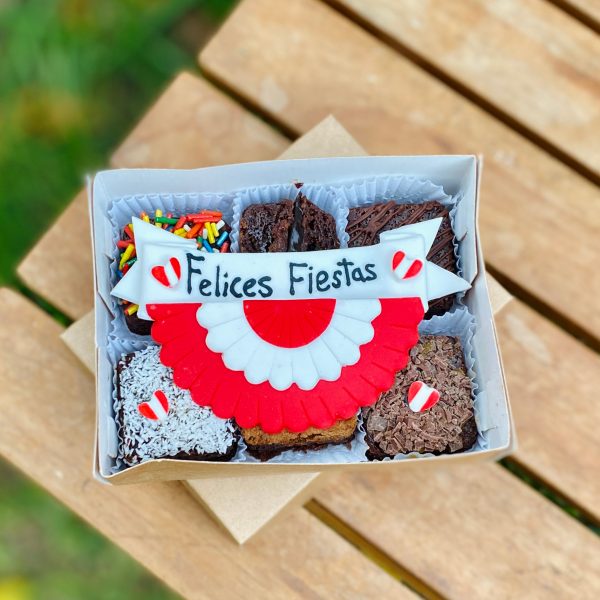 Seis postres decorados con fondant, presentados con una bandera, escarapela y corazones, empaquetados en una caja ecológica con opción de sticker personalizado.