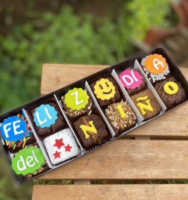 Doce brownies decorados con fondant y toppings variados, empaquetados en una caja marrón vintage con lazo de tela.