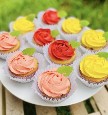 Set de cupcakes decorados con buttercream en diversos colores representando flores, con delicadas hojitas, empaquetados en una caja blanca con ventana.