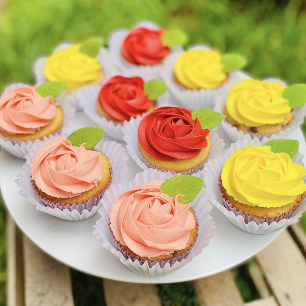 Cupcakes Set de cupcakes decorados con buttercream en diversos colores representando flores, con delicadas hojitas, empaquetados en una caja blanca con ventana.